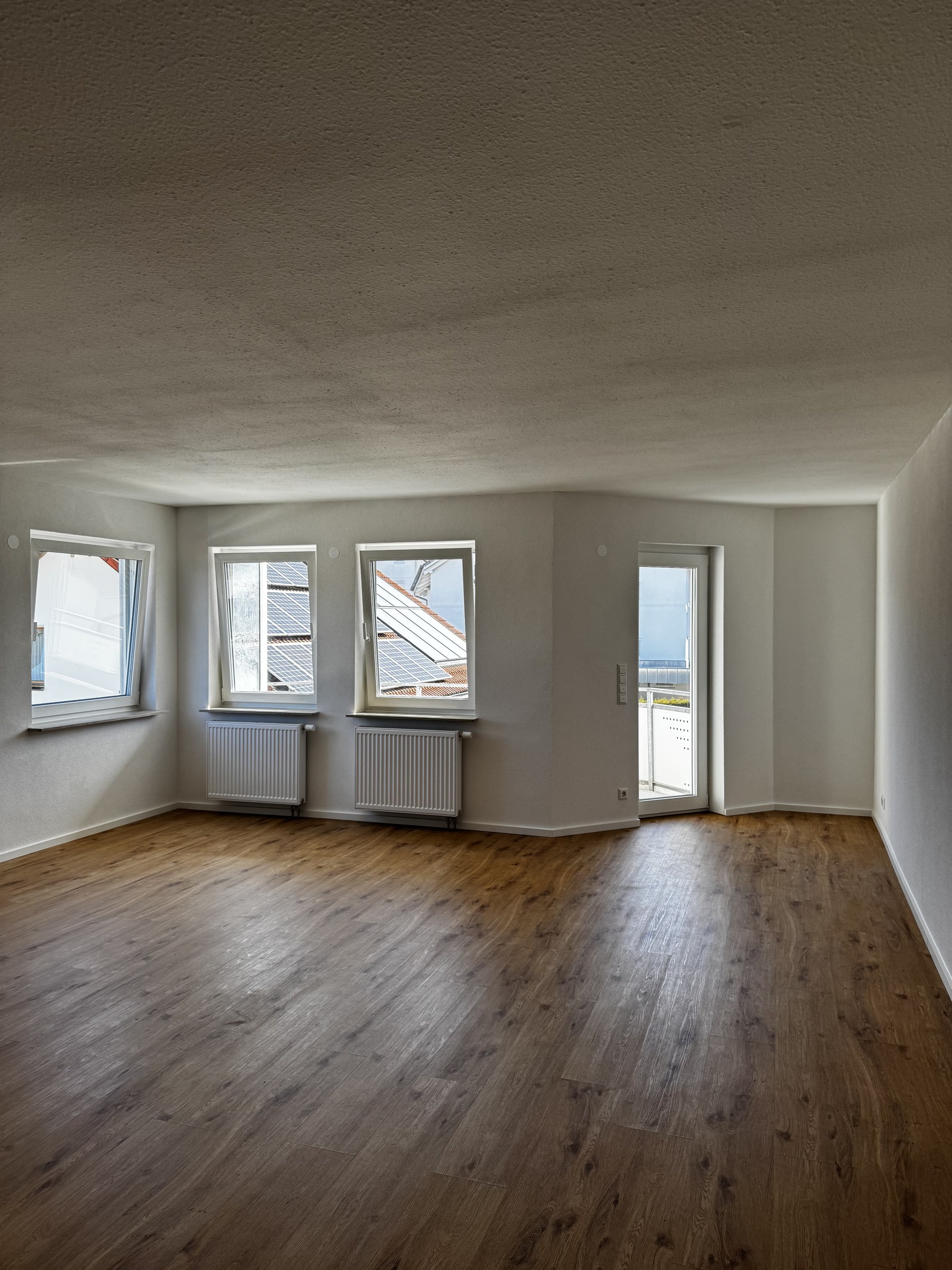 Sanierter Wohnraum mit drei weißen Fenstern und Balkontür